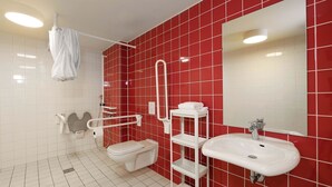 A modern bathroom with red tiled walls, a white toilet, a white sink, and a white shelf unit. - B&B Hotel Berlin-Alexanderplatz (Berlin)