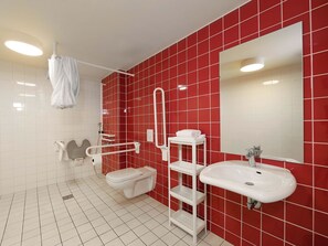A modern bathroom with red tiled walls, a white toilet, a white sink, and a white shelf unit. - B&B Hotel Berlin-Alexanderplatz (Berlin)