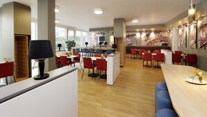 A modern restaurant with wooden flooring, red and blue chairs, and a central counter. - B&B Hotel Berlin-Alexanderplatz (Berlin)