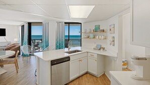 A modern kitchen with a dishwasher, white cabinets, and a view of the sea.
