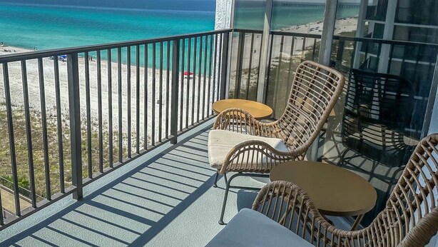 A balcony with wicker furniture, a glass railing, and a view of the beach and ocean.
