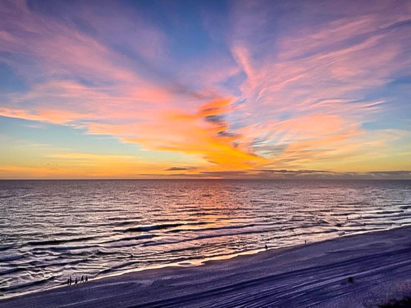 Una playa con un atardecer sobre el océano, mostrando un cielo despejado y aguas tranquilas.