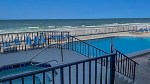 A pool area with a view of the ocean, a fenced deck, and lounge chairs.