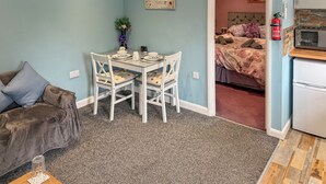 Une pièce compacte comprenant une table et des chaises, un canapé, un lit avec une literie à motifs floraux et un coin cuisine.