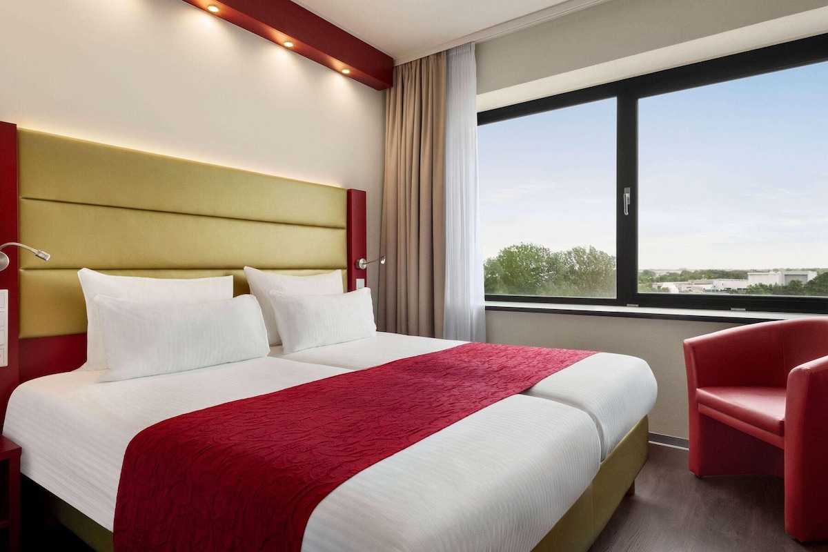 Une chambre d’hôtel avec un grand lit, un fauteuil rouge et une fenêtre donnant sur la ville.
