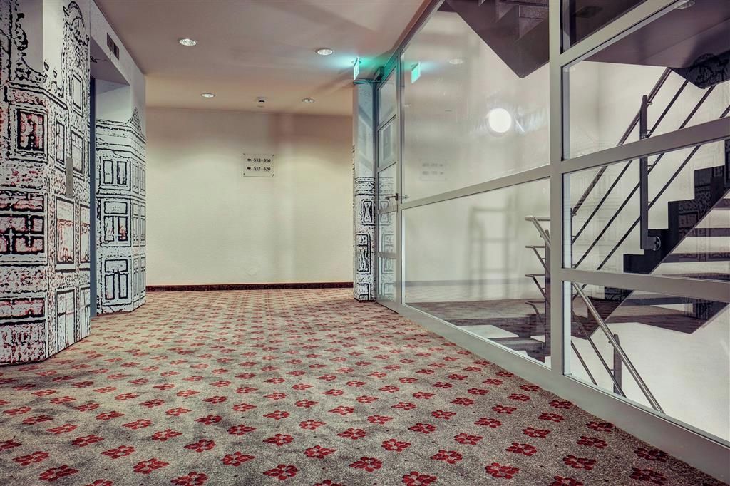 A hallway with patterned carpet, a glass door, and a staircase with metal railings.