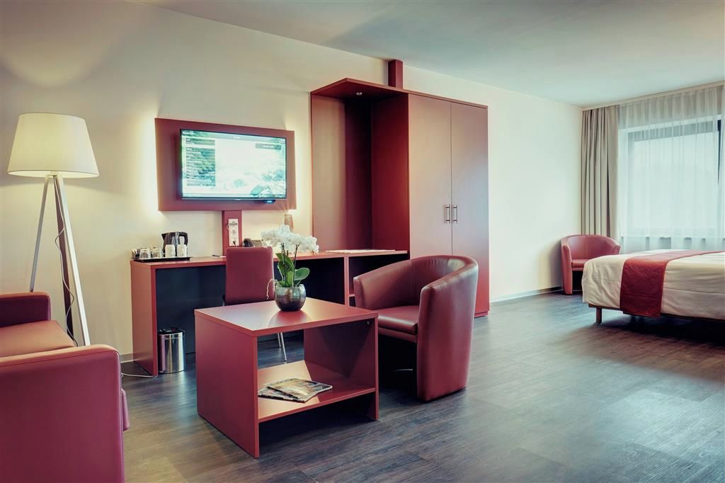 Une chambre d’hôtel avec un lit, un bureau et une chaise, une télévision et un canapé rouge.