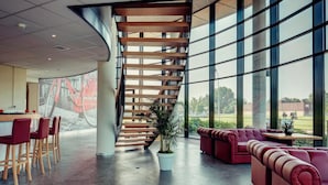 Un interior moderno con una escalera curva, zona de estar y ventanas amplias con vistas al exterior.