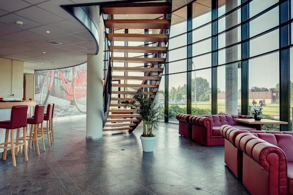 Un intérieur moderne avec un escalier à volutes, un coin salon et de grandes fenêtres offrant une vue sur l’extérieur.