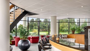 Un área de estar moderna con sillones de cuero, un bar y ventanas amplias que ofrecen vistas a zonas verdes.