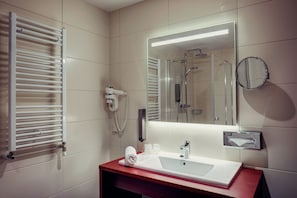Une salle de bain moderne avec un lavabo blanc, un miroir, une serviette et une cabine de douche en verre.