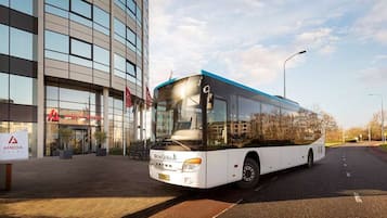 A modern bus parked in front of a hotel with a glass facade.