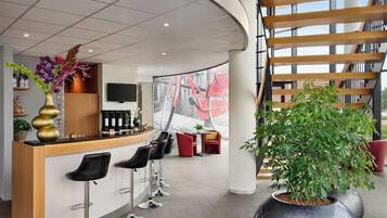 Un espace bar moderne avec un comptoir incurvé, des tabourets de bar et une grande plante en pot.