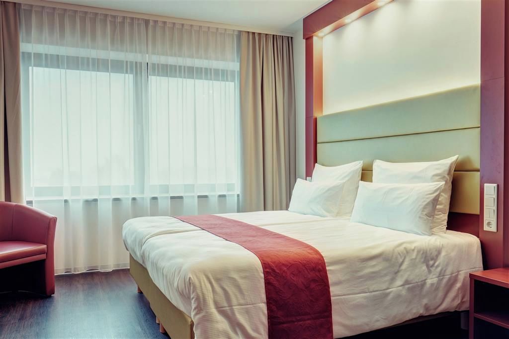 A hotel room with a large bed, a bedside table, a chair, and a window with curtains.