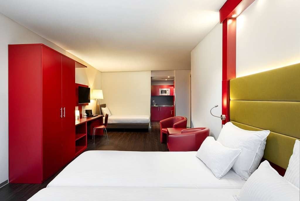 A hotel room with a bed, a desk, a chair, and a red wardrobe.