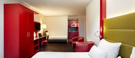A hotel room with a bed, a desk, a chair, and a red wardrobe.