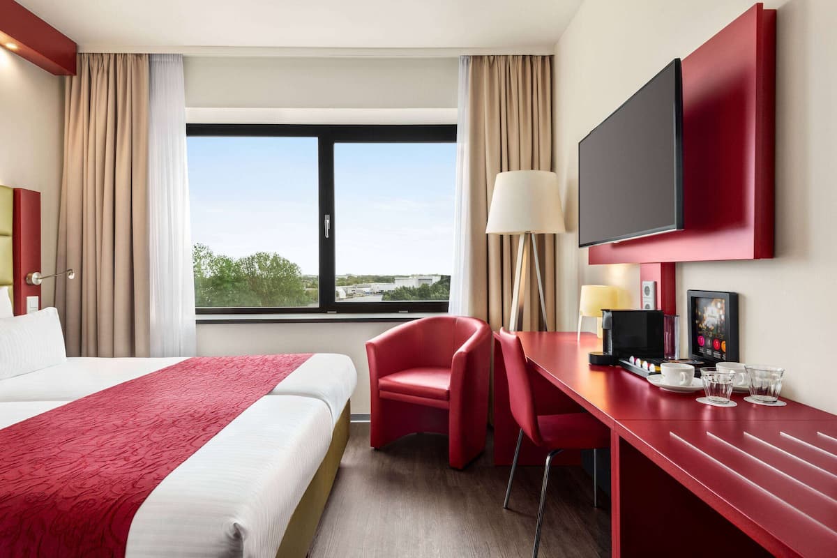 Une chambre d’hôtel avec un grand lit, un bureau équipé d’une machine à café, une télévision et une vue sur l’extérieur.