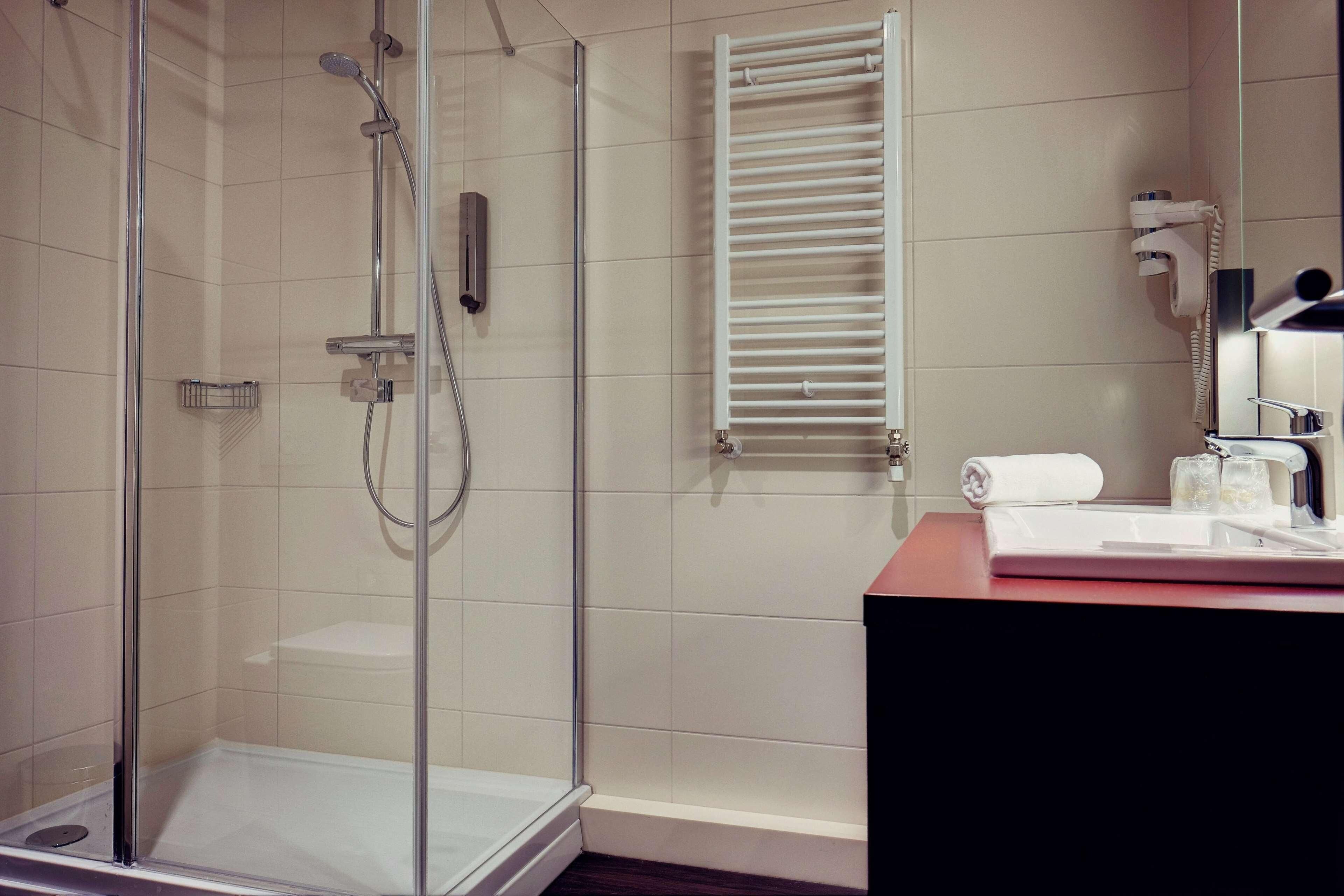 A modern bathroom with a glass-enclosed shower, a white towel, a hairdryer, and a sink with a mirror.
