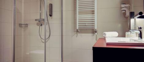 A modern bathroom with a glass-enclosed shower, a white towel, a hairdryer, and a sink with a mirror.