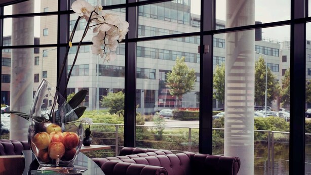 Un interior moderno con una mesa de vidrio, un florero con flores y una vista de la ciudad a través de grandes ventanales.