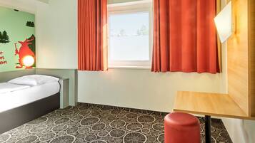 Ein Hotelzimmer mit einem Bett, einem Fenster mit Vorhängen, einem gemusterten Boden und einem kleinen Tisch.