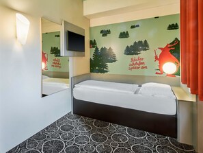 Habitación de hotel con cama, televisor de pared y un mural con siluetas de bosque y montañas.