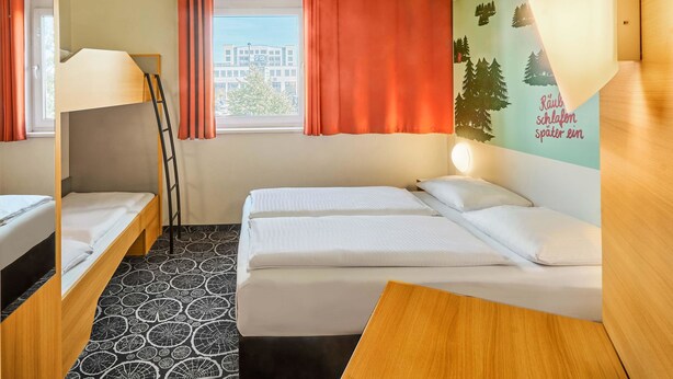 Habitación de hotel con literas, una cama individual, un escritorio y un ventanal con cortinas.