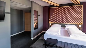 Una habitación de hotel moderna con una cama grande, mesitas de noche, un televisor de pantalla plana y un diseño de pared geométrico original.