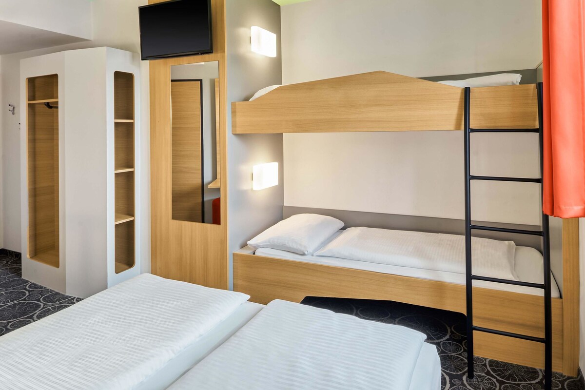 Una habitación de hotel con literas, un armario, un televisor y una mesita de noche.