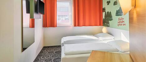 Habitación de hotel con cama, una mesita, televisor montado en la pared y ventana con cortinas.