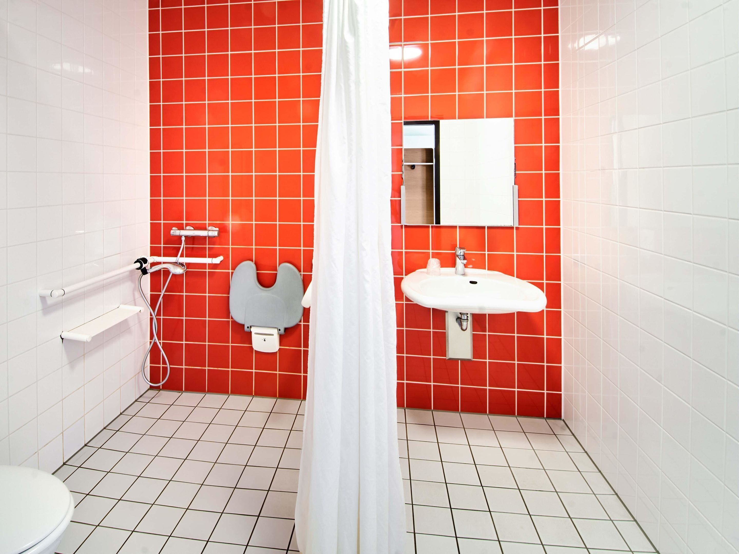 Ein Badezimmer mit roten Fliesen, einem weißen Waschbecken, einem Spiegel und einer Duschvorhang.