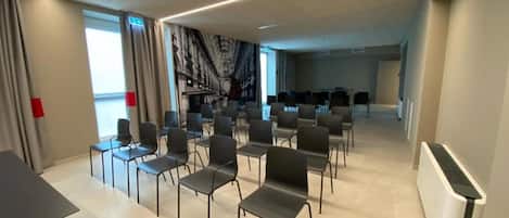 A conference room with rows of chairs, a whiteboard, and a large window with curtains.