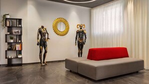 A modern living room with a grey sofa, a red accent cushion, a black bookshelf with decorative items, and two wall-mounted sculptures. - Amedia Milano - Trademark Collection by Wyndham (Milan)