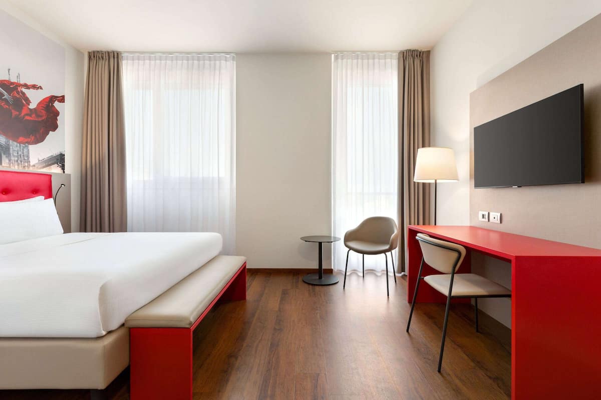 Une chambre d’hôtel comprenant un lit, un bureau avec une chaise, une télévision et une lampe.