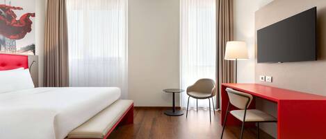 Ein Hotelzimmer mit einem Bett, einem Schreibtisch mit Stuhl, einem Fernseher und einer Lampe.