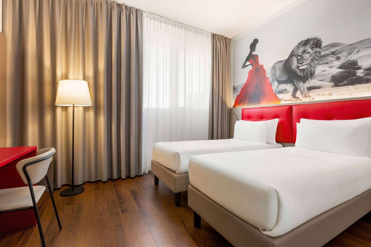 Une chambre d’hôtel avec deux lits, un bureau, une chaise et une lampe.
