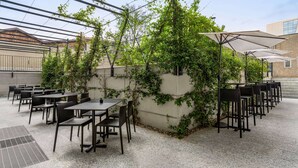 An outdoor patio with tables and chairs, covered by umbrellas, and surrounded by greenery. - Amedia Milano - Trademark Collection by Wyndham (Milan)