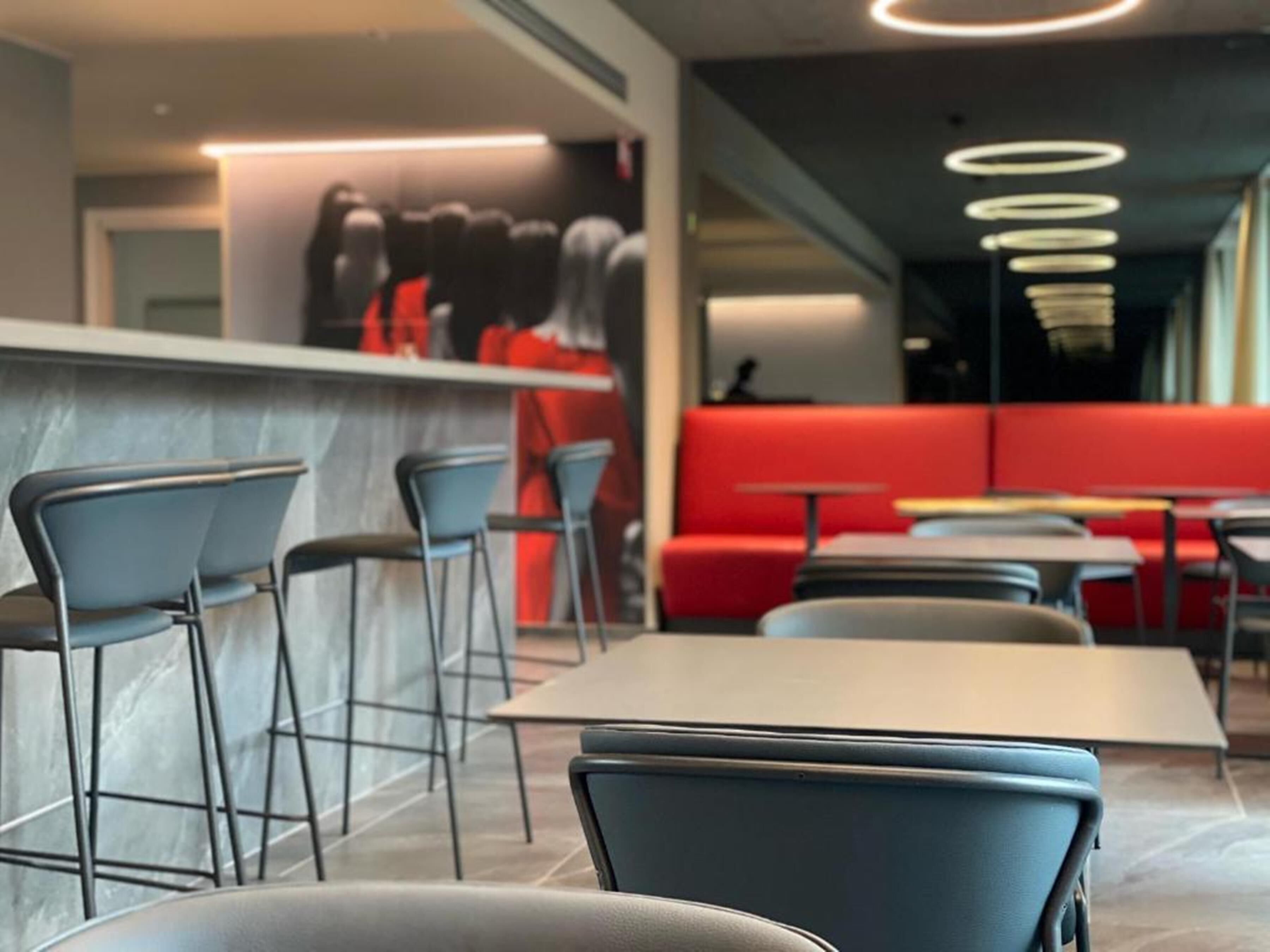 A modern restaurant interior with bar seating, high tables, and red booths.