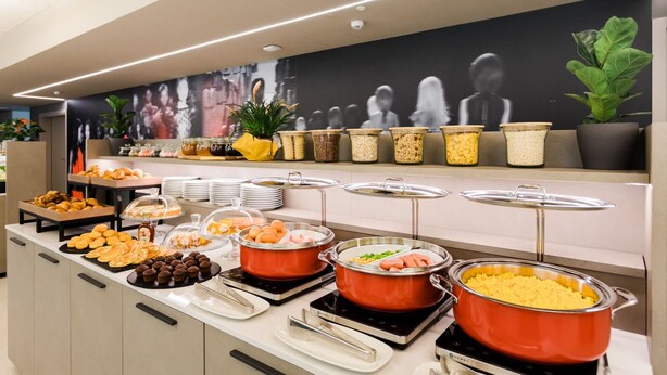 A buffet with various food items, including pastries, fruits, and cooked dishes, arranged on a counter with a modern design. - Amedia Milano - Trademark Collection by Wyndham (Milan)