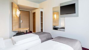 Habitación de hotel con dos camas, un televisor montado en la pared, un armario y un escritorio con lámpara.