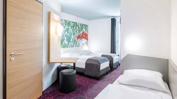 Une chambre d’hôtel avec une porte en bois, un lit avec du linge de lit blanc, une petite table et une peinture abstraite aux couleurs vives accrochée au mur.