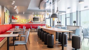 Un restaurante moderno con una barra alargada, asientos rojos y ventanas amplias.