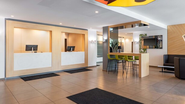 Un área de recepción moderna con dos mostradores, una zona de bar con taburetes y un espacio de estar con un sofá.