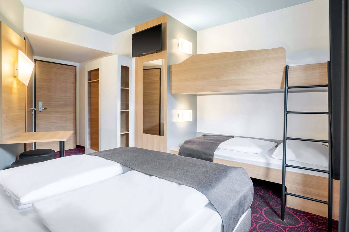 A hotel room with two beds, a TV, a wardrobe, and a desk.