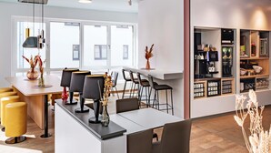 A modern dining area with a long table, multiple chairs, and a bar counter. - B&B Hotel Hildesheim (Hildesheim)