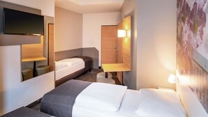 A hotel room with a bed, a desk, a chair, a TV, and a wall-mounted light. - B&B Hotel Hildesheim (Hildesheim)