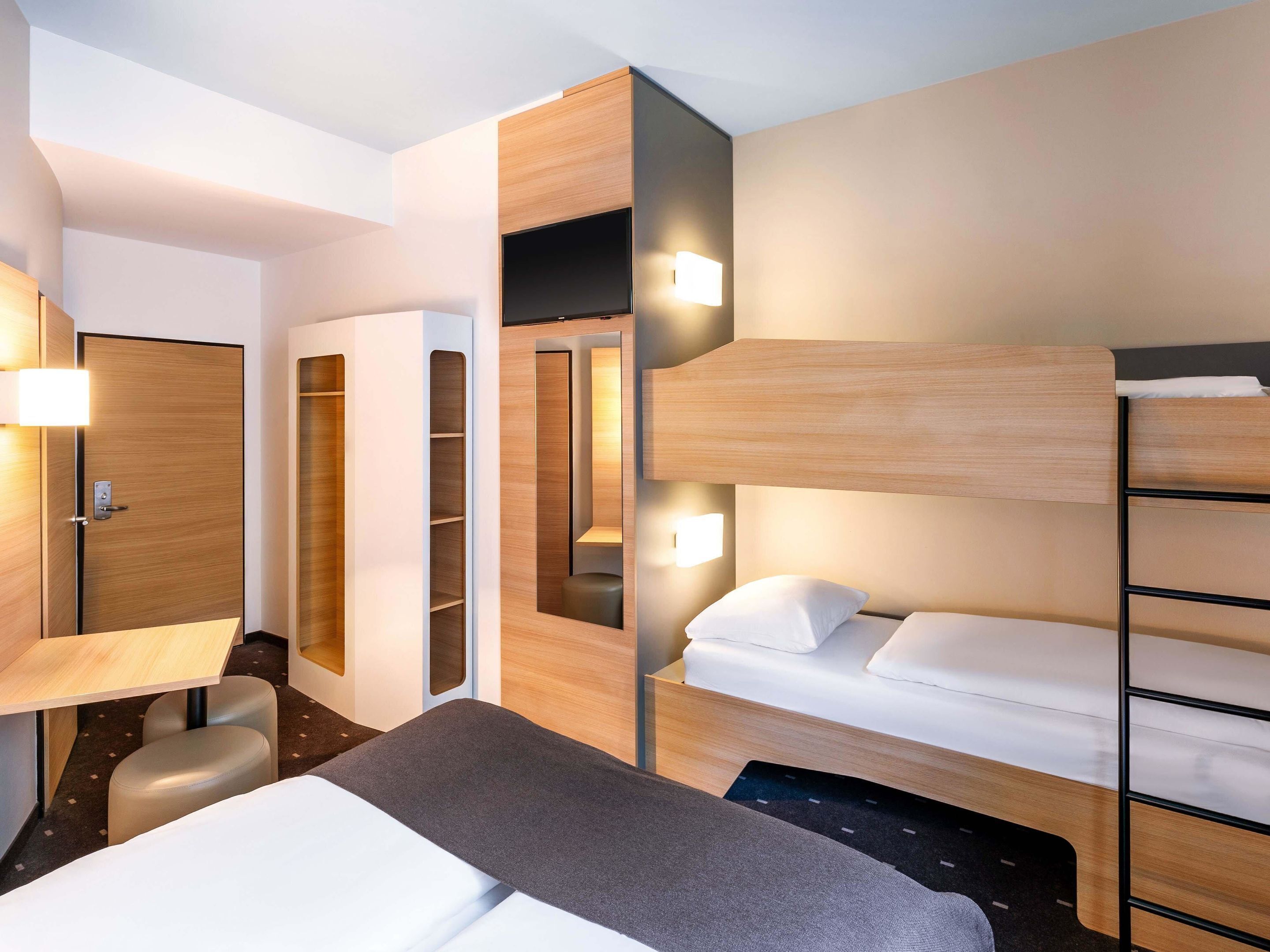 Une chambre d’hôtel moderne équipée d’un lit superposé, d’un bureau et d’une armoire.