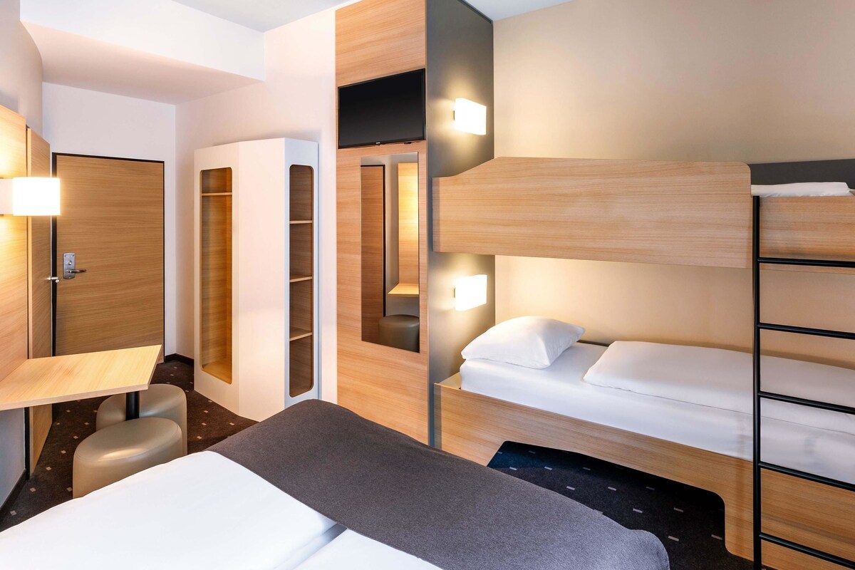 A modern hotel room with a bunk bed, a desk, and a wardrobe.