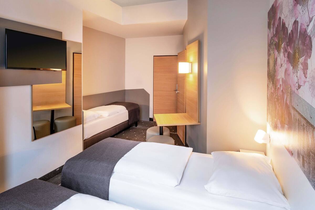 Ein Hotelzimmer mit Bett, Schreibtisch, Stuhl, Fernseher und Wandleuchte.