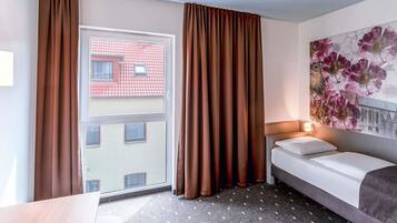 Une chambre d’hôtel avec un lit, un bureau, une fenêtre avec des rideaux et une décoration murale à motifs floraux.
